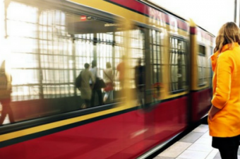 mulher de casaco amarelo olha trem passando em estação