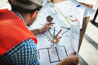 Engenharia / pessoa com chapéu de construção examinando uma planta de edifício