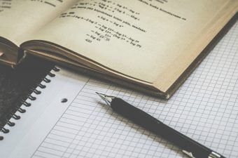 Lapiseira, caderno e um livro de matemática aberto