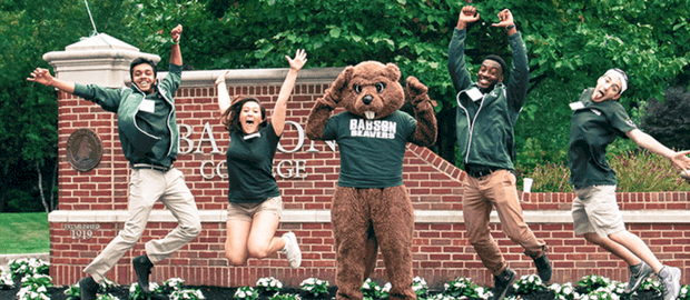 estudantes de graduação em Babson College saltam em frente aos portões da universidade