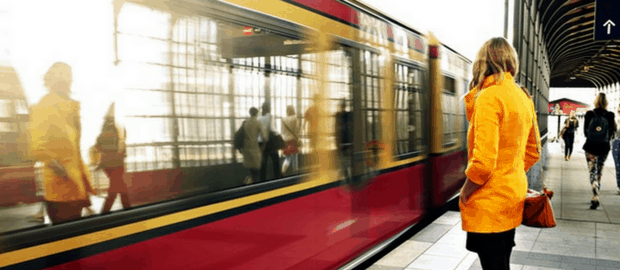 mulher de casaco amarelo olha trem passando em estação