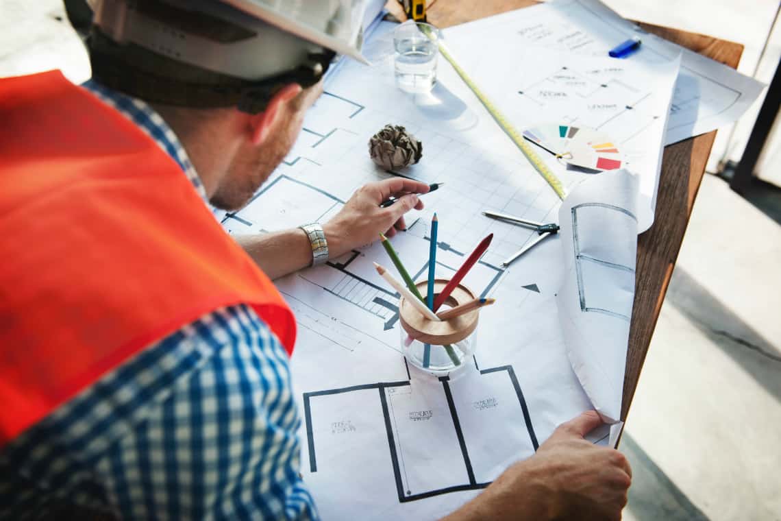 Engenharia / pessoa com chapéu de construção examinando uma planta de edifício