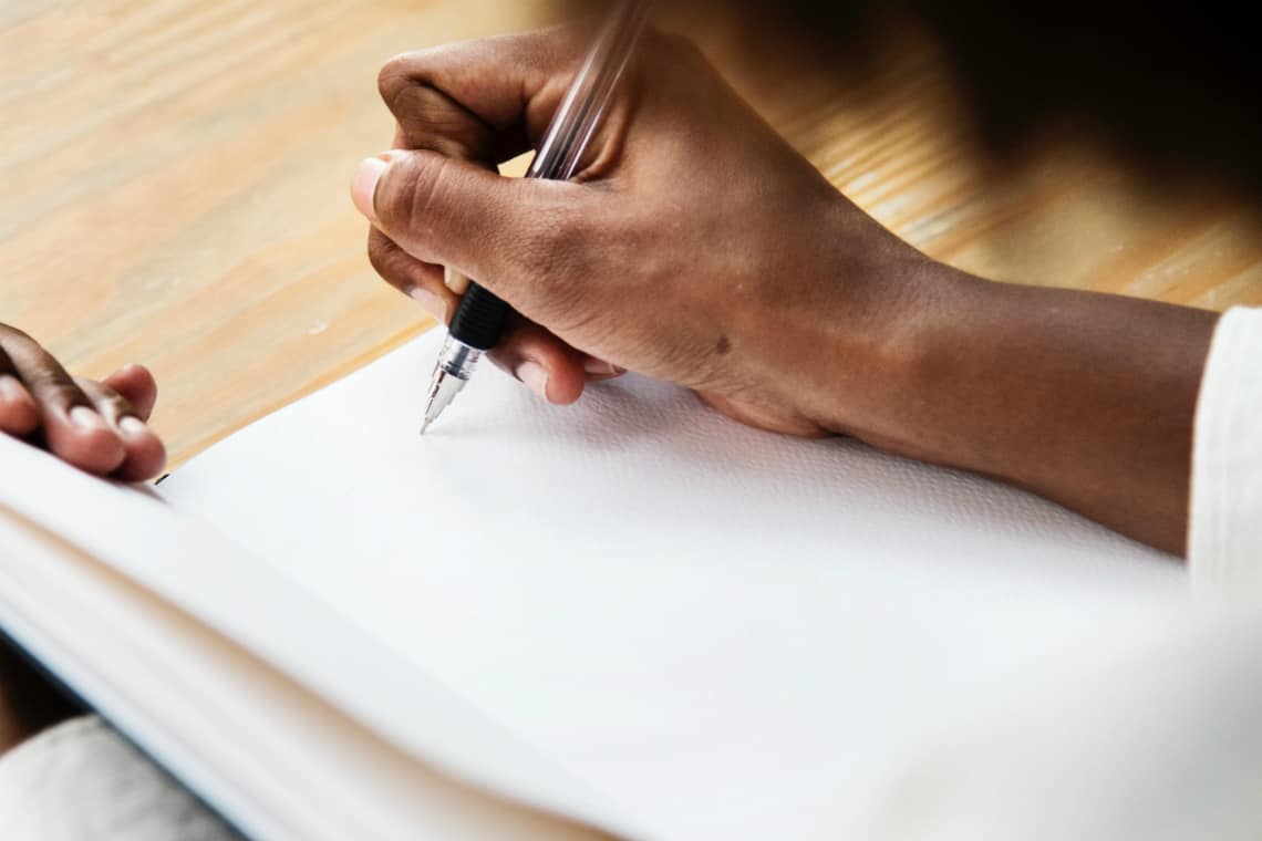 Mulher segurando um caderno aberto e uma caneta numa página em branco