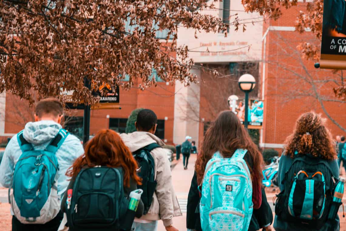 Cinco estudantes com mochilas, de costas, andando