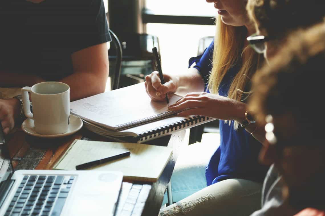 Quatro pessoas sentadas em torno de um caderno no canto de uma mesa