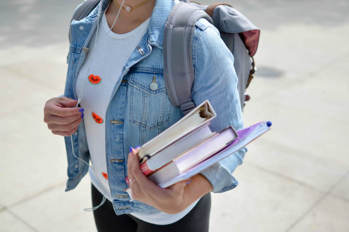 Menina com mochila nas costas e fichário e livros nas mãos