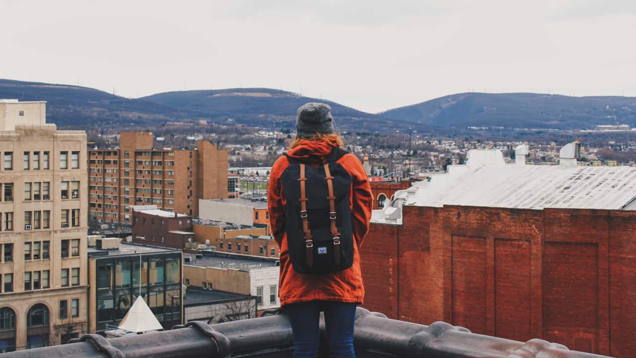 pessoa de mochila em uma varando olhando para uma cidade - como estudar no exterior