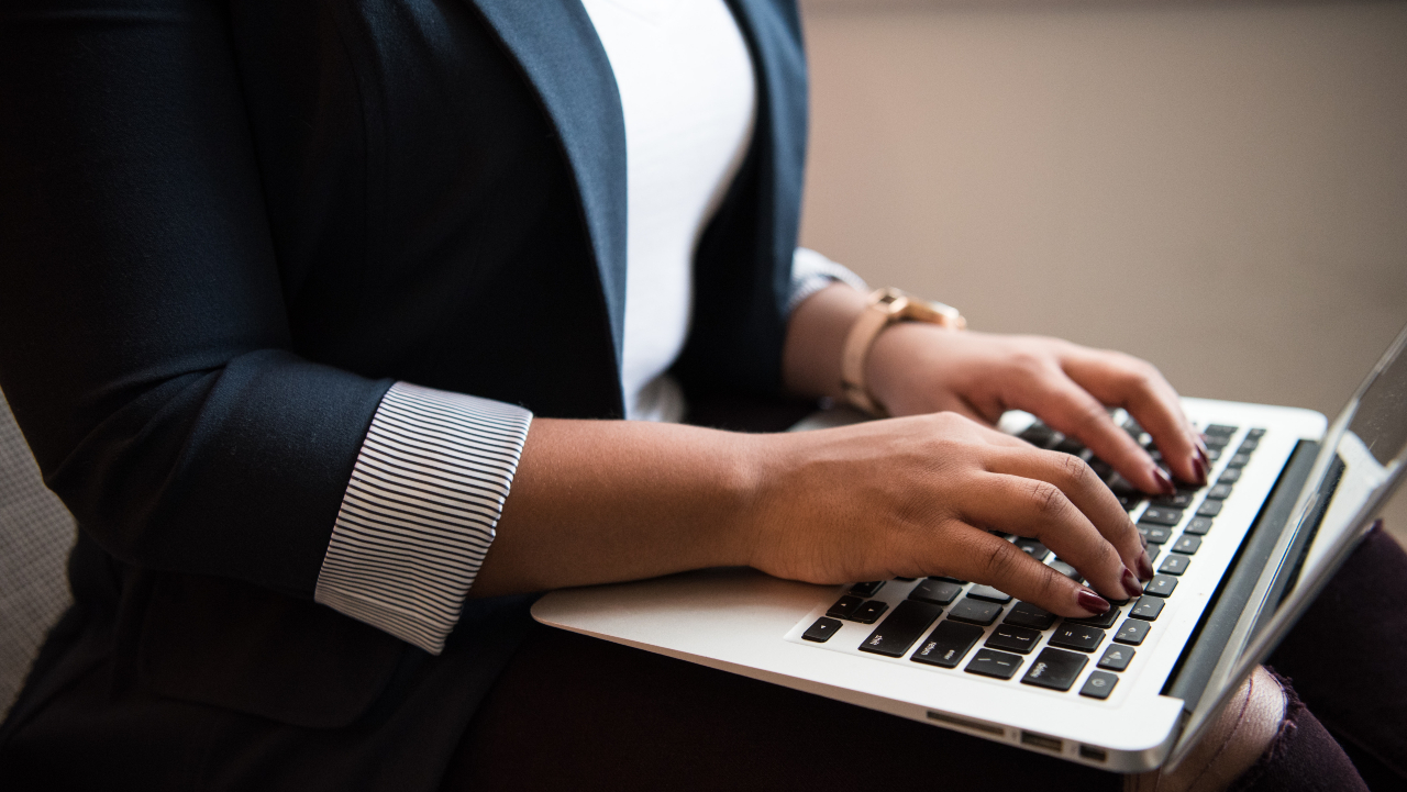 Moça de roupa formal escrevendo num macbook. - bolsa de mba para mulheres