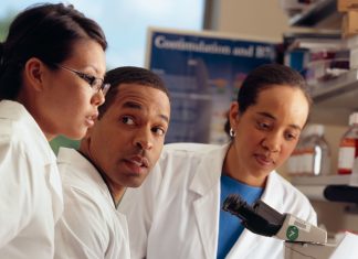 Três pessoas de jaleco olhando um microscópio - carreira acadêmica