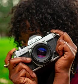 Pessoa de cabelo enrolado atrás de uma câmera pentax - estudar fotografia em Nova York