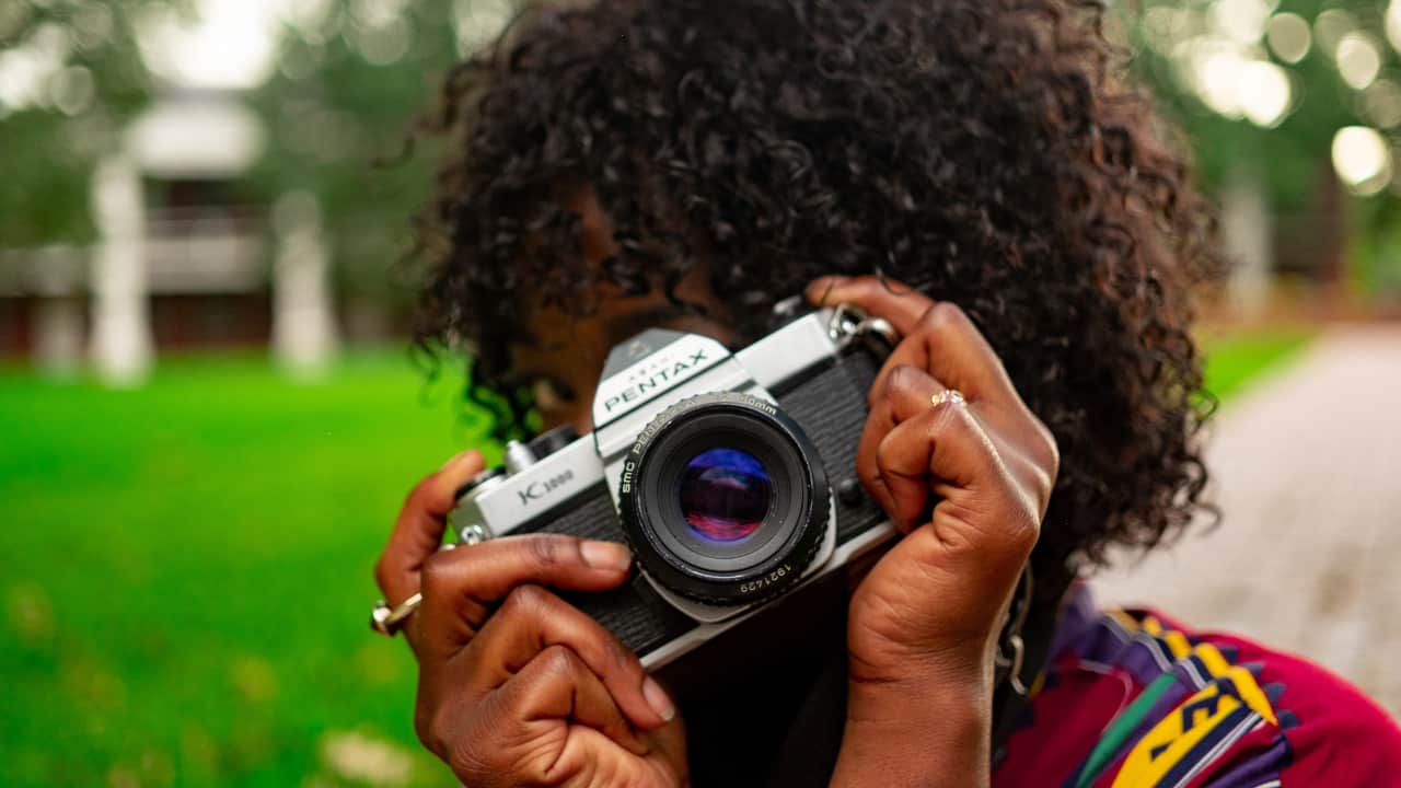 Pessoa de cabelo enrolado atrás de uma câmera pentax - estudar fotografia em Nova York