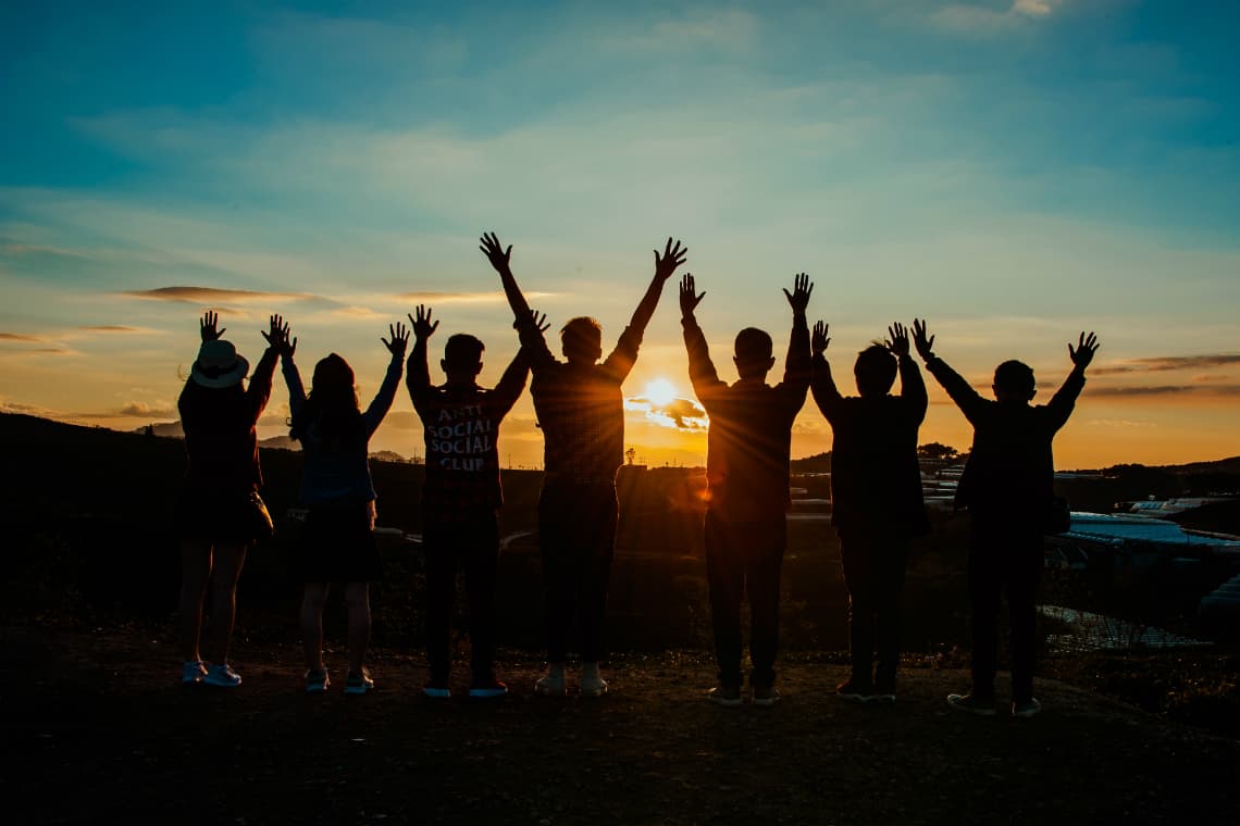 Direitos Humanos - pessoas com as mãos para cima olhando um por do sol