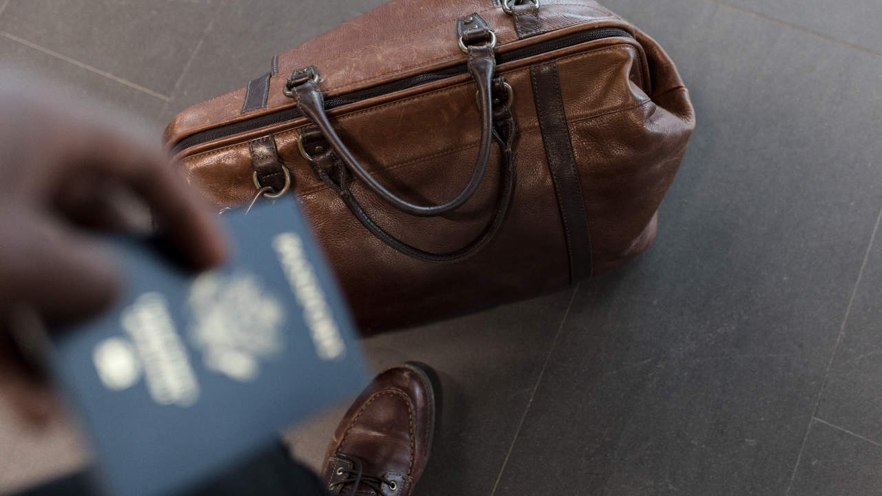 Pessoa segurando passaporte e uma mala no chão - apoio financeiro para estudar fora