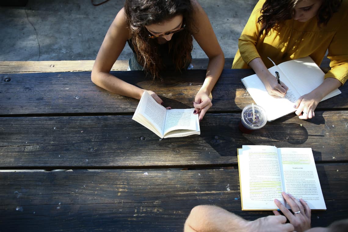 três mulheres estudando numa mesa de madeira