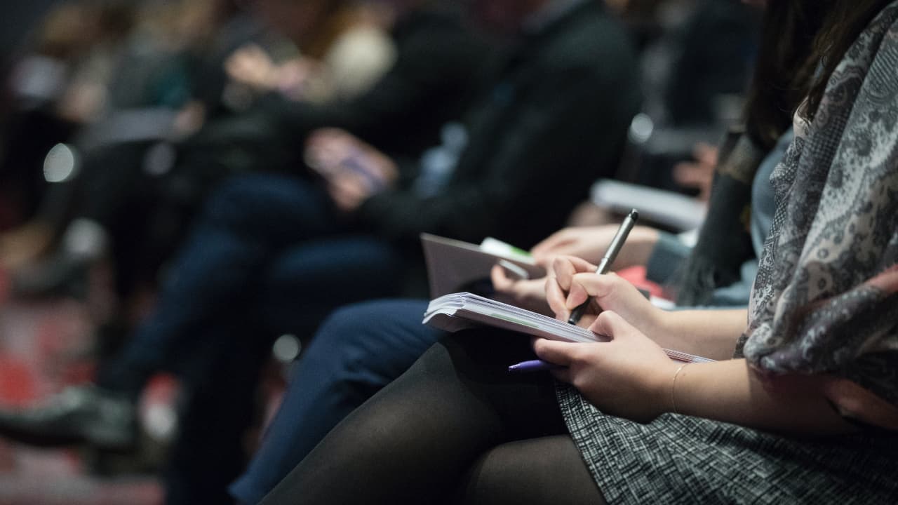 Moça sentada de pernas cruzadas escrevendo num bloquinho em um evento para imprensa - bolsas para jornalistas