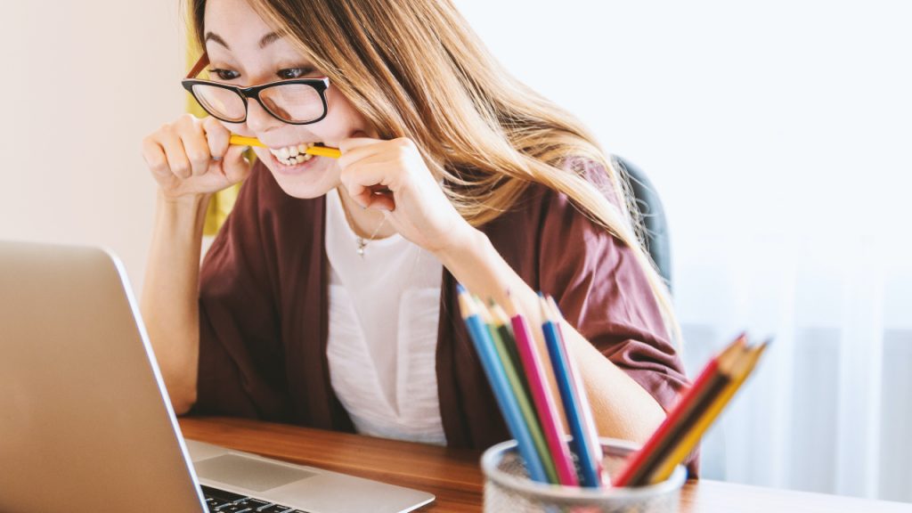 Moça mordendo um lápis olhando para o computador - TOEFL em casa