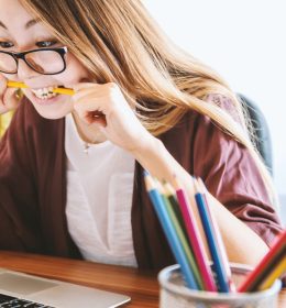 Moça mordendo um lápis olhando para o computador - TOEFL em casa