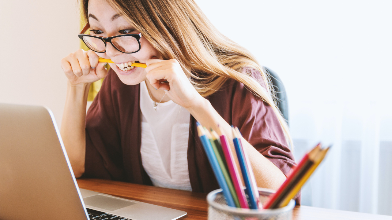Moça mordendo um lápis olhando para o computador - TOEFL em casa