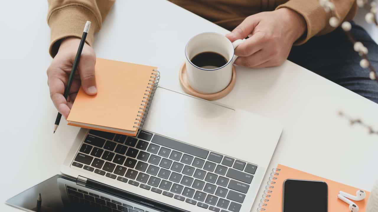 pessoa em frente ao notebook com bloquinho numa mão e café na outra - foro brasil españa