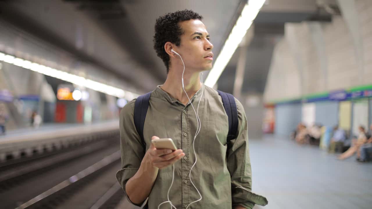 Pessoa no metrô com celular na mão e fones de ouvido - vídeos sobre estudar fora