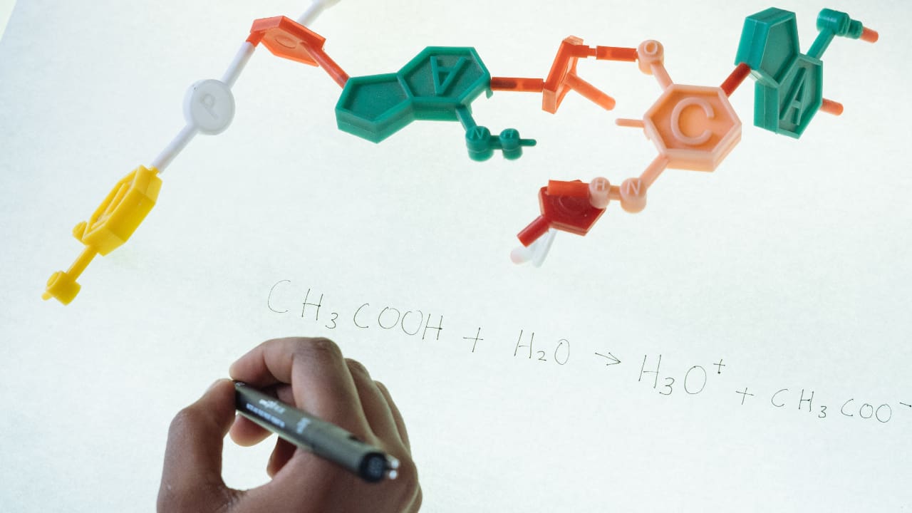 Mão escrevendo num quadro iluminado, com um esquema representando uma molécula em cima - mestrado em nanomedicina