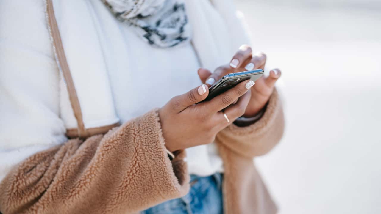 Moça segurando um celular com as duas mãos - apps mais baixados