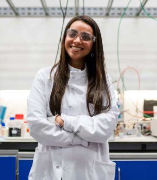 Moça sorridente de jaleco no laboratório olhando para a câmera - bolsas para mulheres nas áreas de ciências