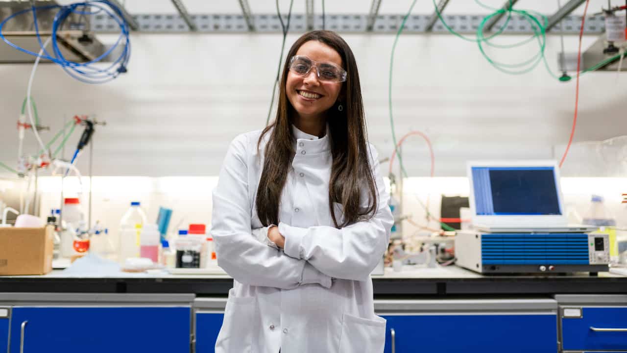 Moça sorridente de jaleco no laboratório olhando para a câmera - bolsas para mulheres nas áreas de ciências