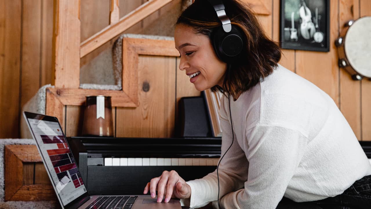 Moça com fones de ouvido mexendo num notebook em frente a um piano - bolsas para músicos