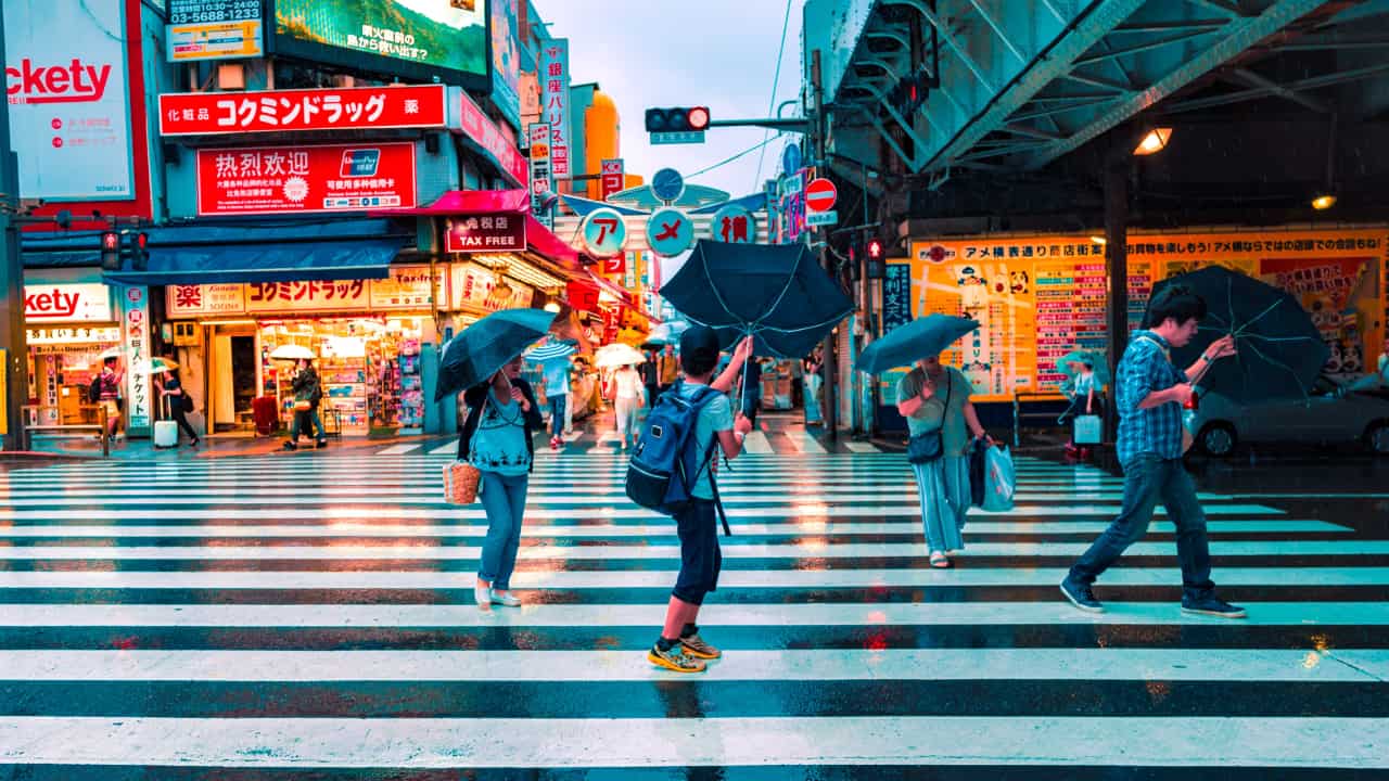 Pessoa atravessando a rua no Japão segurando um guarda-chuva que parece querer fugir de suas mãos