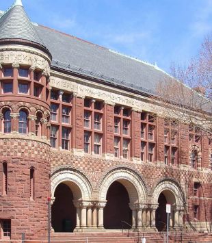 Entrada do Austin Hall da Faculdade de Direito de Harvard. O prédio é construído com tijolos antigos alaranjados e uma entrada com três grandes arcos.
