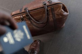 Pessoa segurando passaporte e uma mala no chão - apoio financeiro para estudar fora